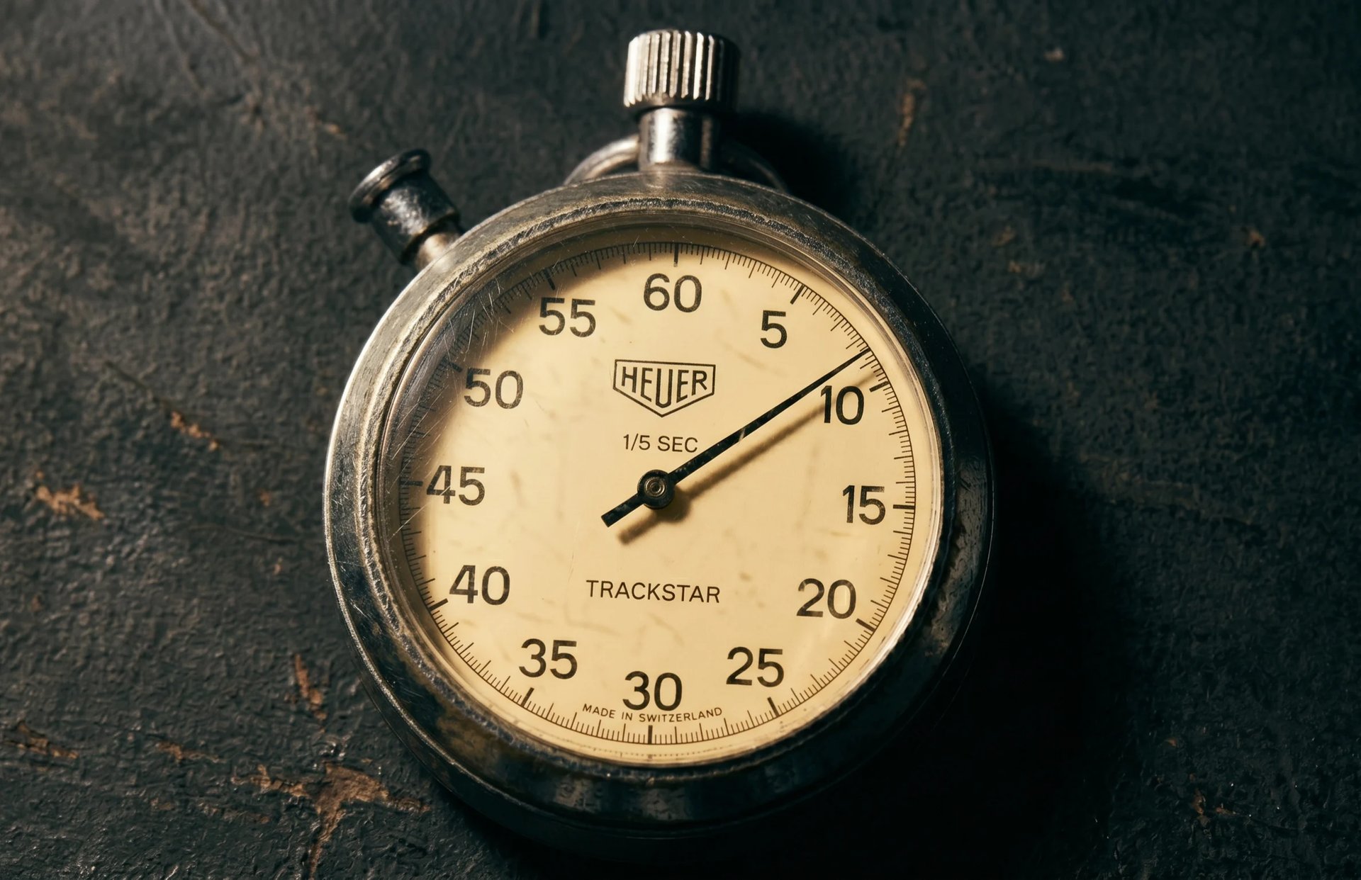 Heuer Trackstar stopwatch on dark textured background showing approximately 12 seconds elapsed time
